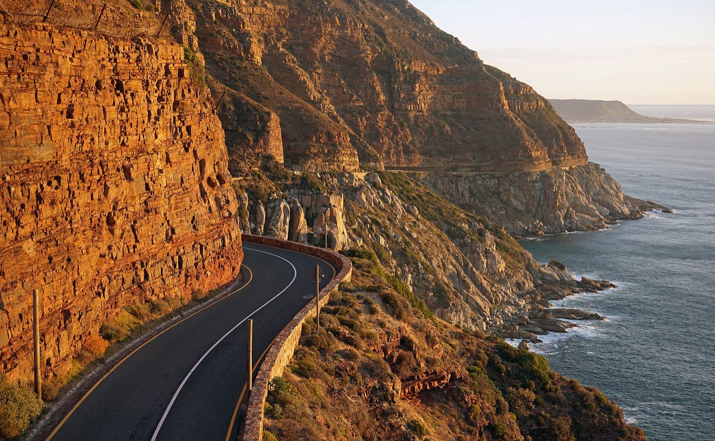 Chapman's Peak Drive curving around the cliff face in low golden light, the Atlantic below to the right.