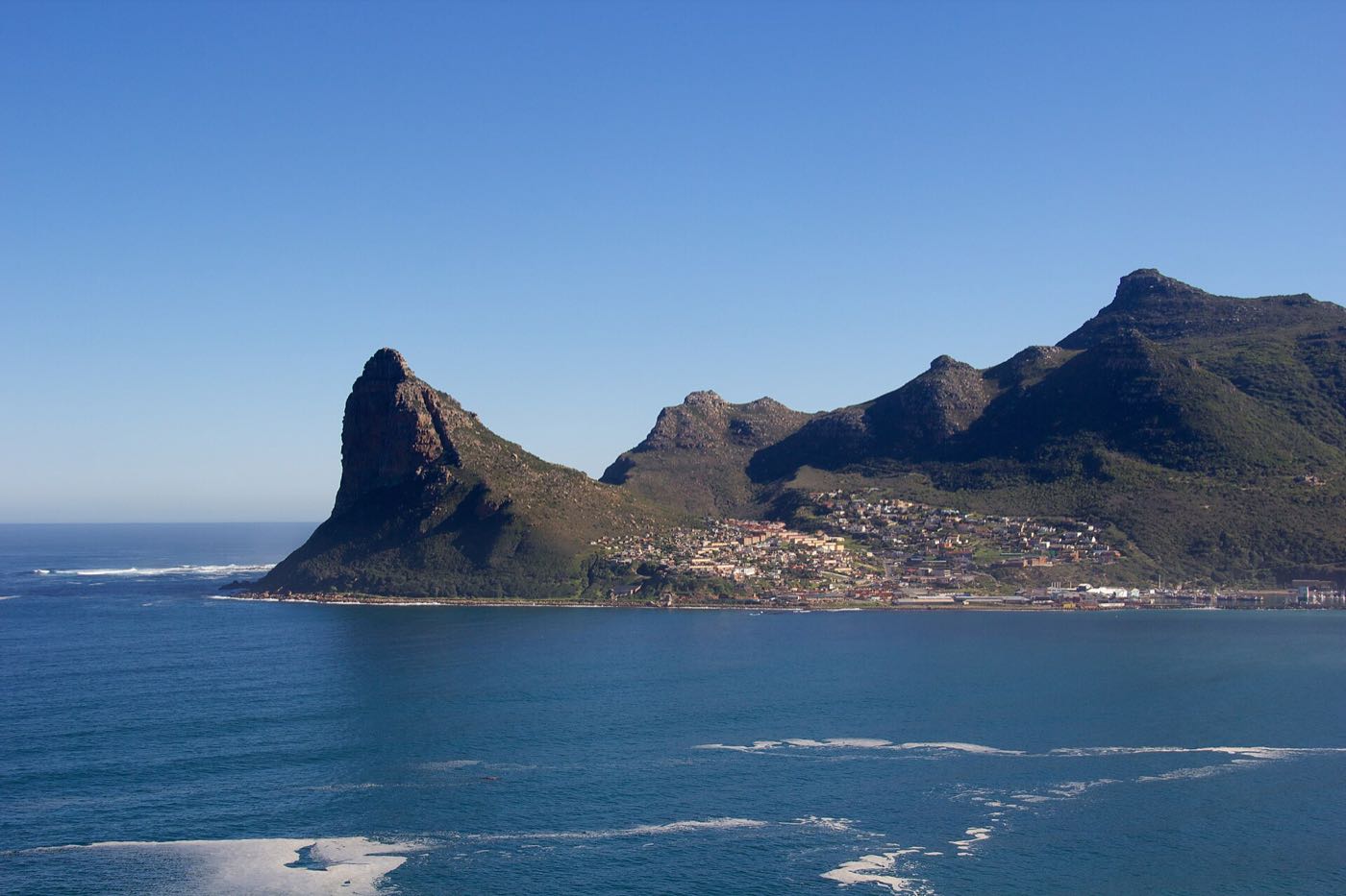 Hout Bay seen from above, with the Sentinel on the left, the village along the shore and the mountains of the valley behind.