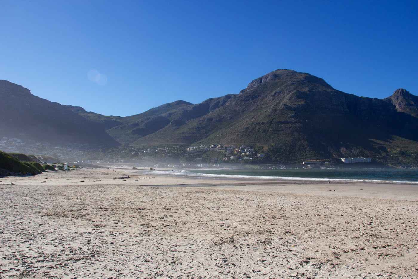 The wide flat sand of Hout Bay beach at low tide, with the mountains of the valley behind.